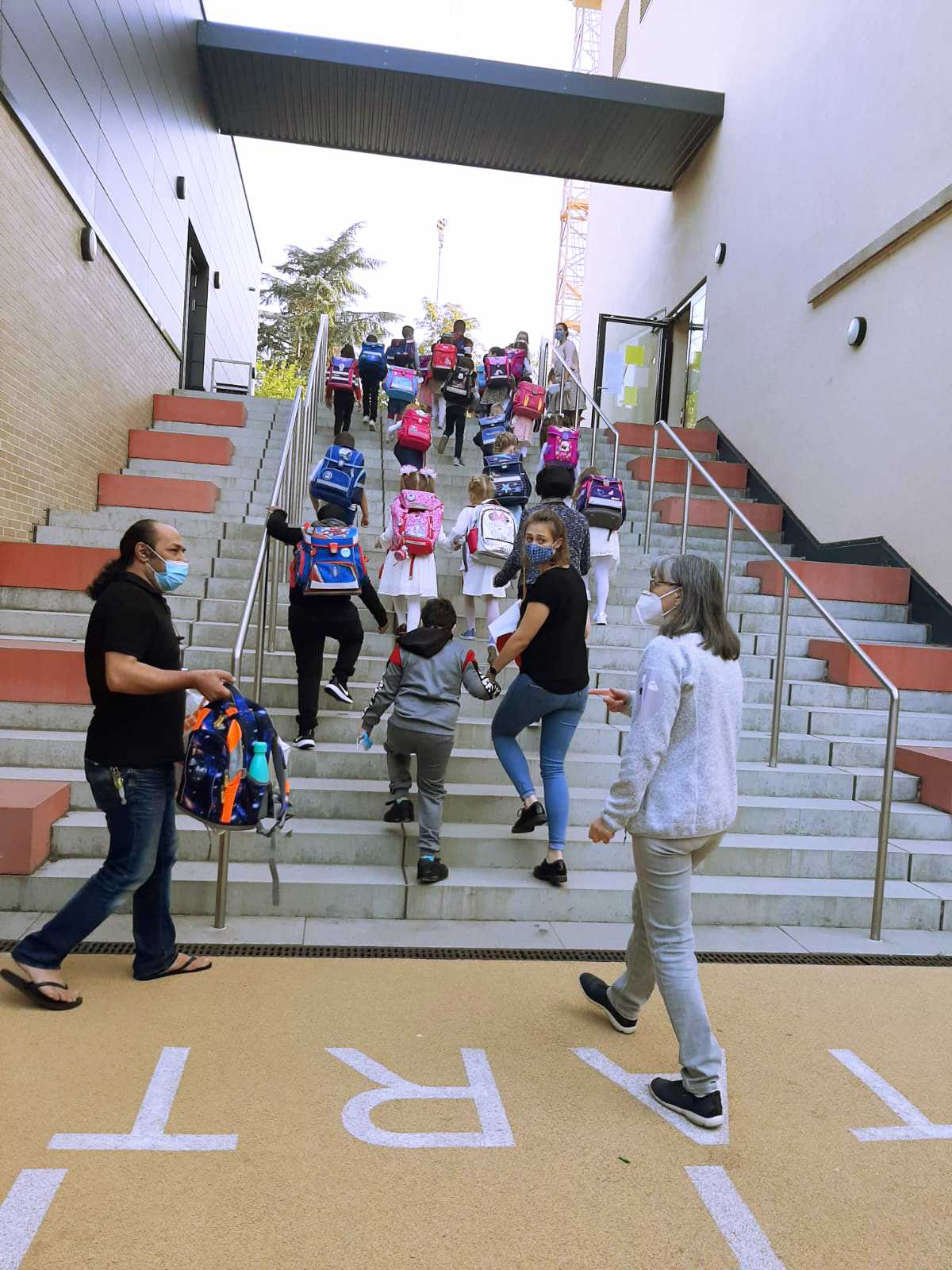 Auf diesem Bild sehen Sie Erstklässler und Erstklässlerinnen mit ihren Schulranzen, wie sie gerade eine Treppe hochlaufen.