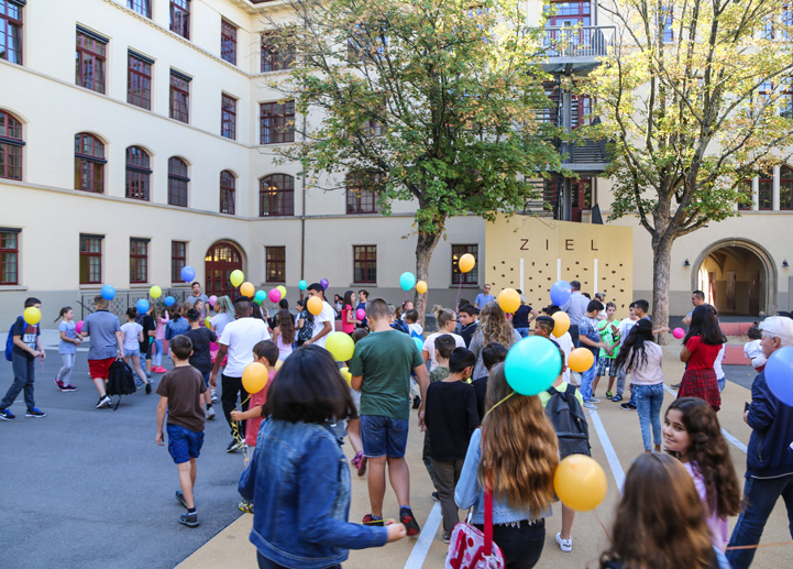 Auf diesem Foto ist ein Schulfest im Innenhof der Nordstadtschule abgebildet. Die Schülerinnen und Schüler freuen sich über bunte Luftballons.