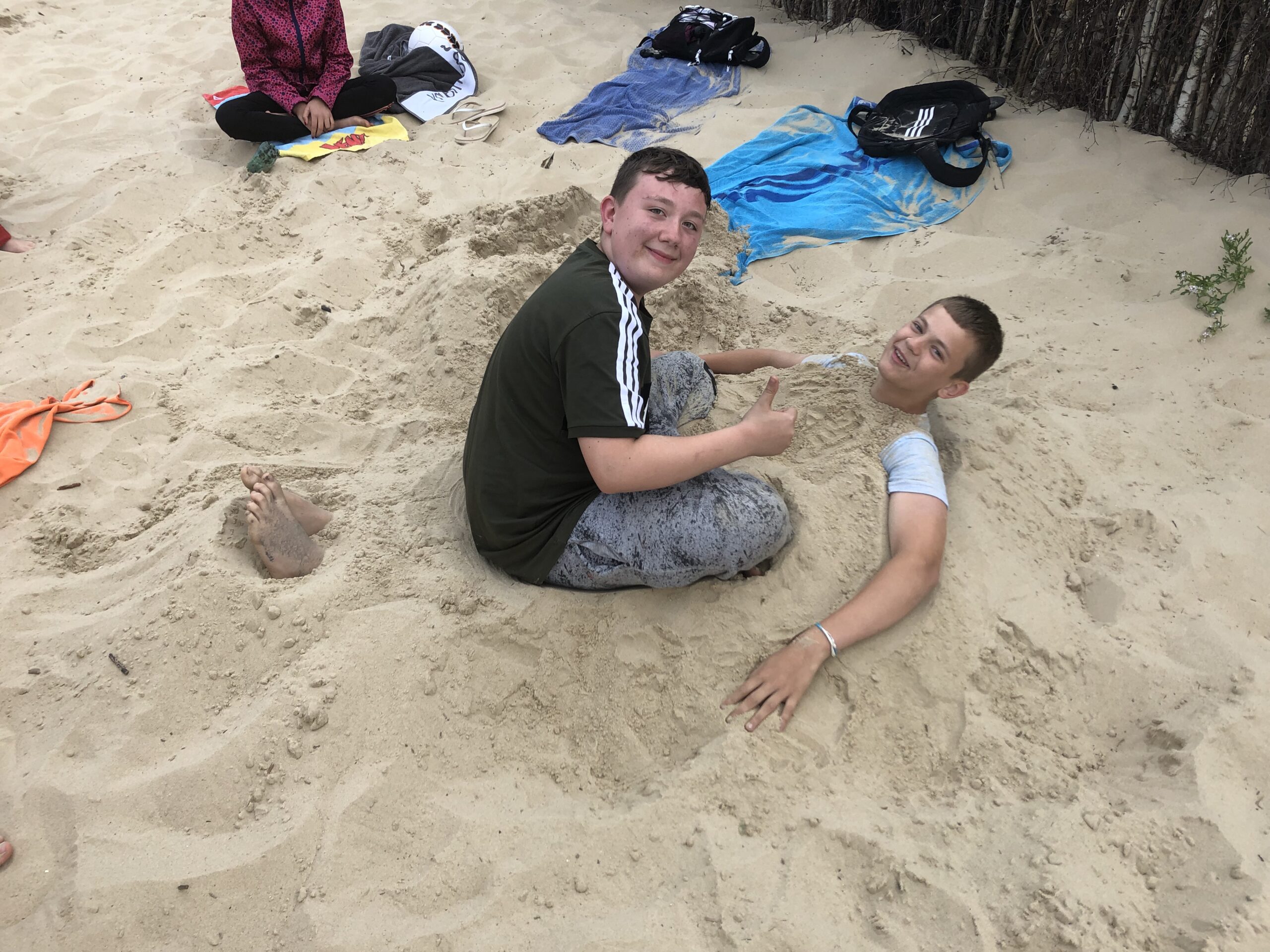 Auf diesem Foto sehen Sie Schüler eingebuddelt im Sand am Strand in Hamburg