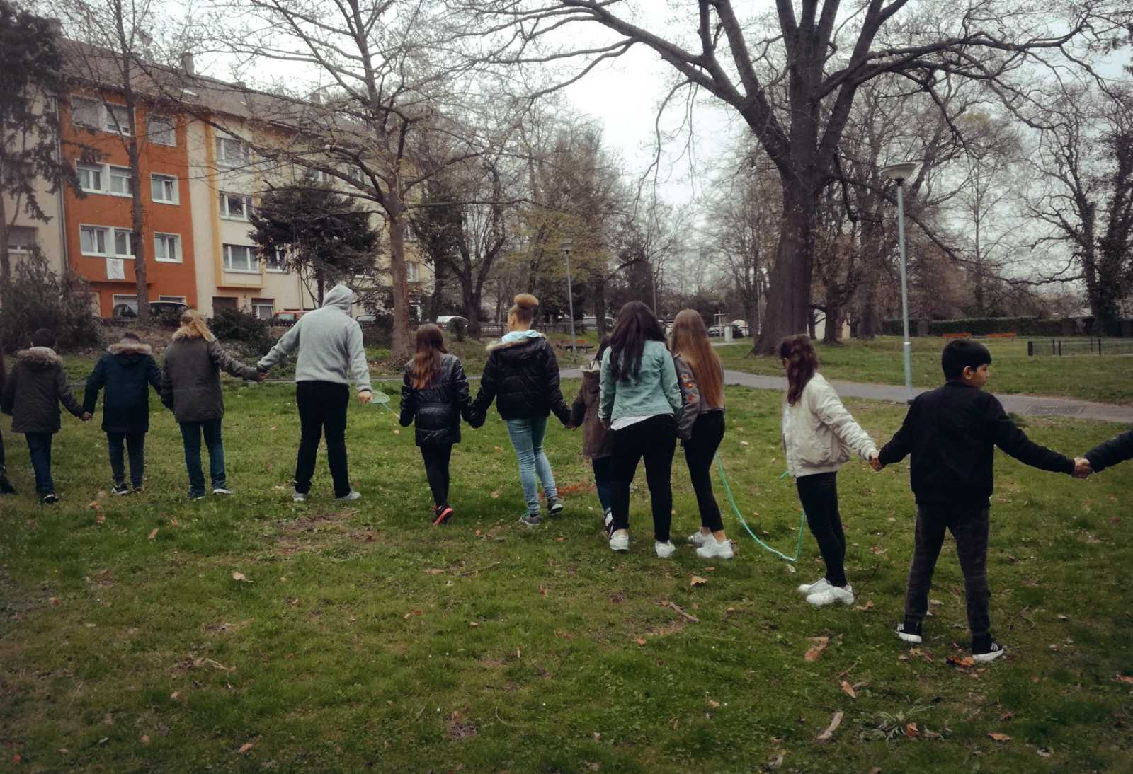 Auf diesem Bild sehen Sie Schülerinnen und Schüler Hand in Hand beim Spielen im Oststadtpark.