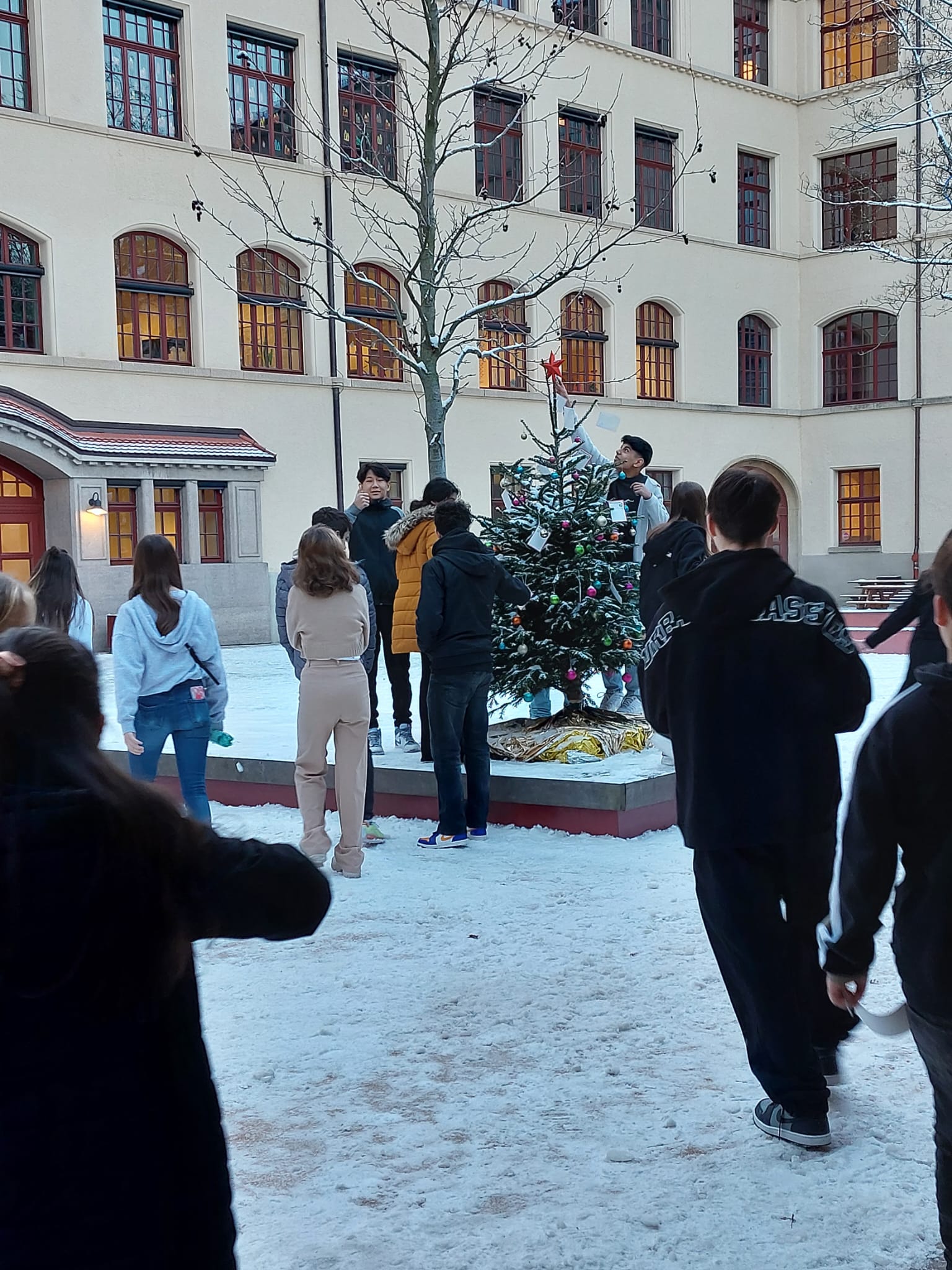 Schülerinnen und Schüler schmücken den Weihnachtsbaum im Schulhof mit ihren Wünschen