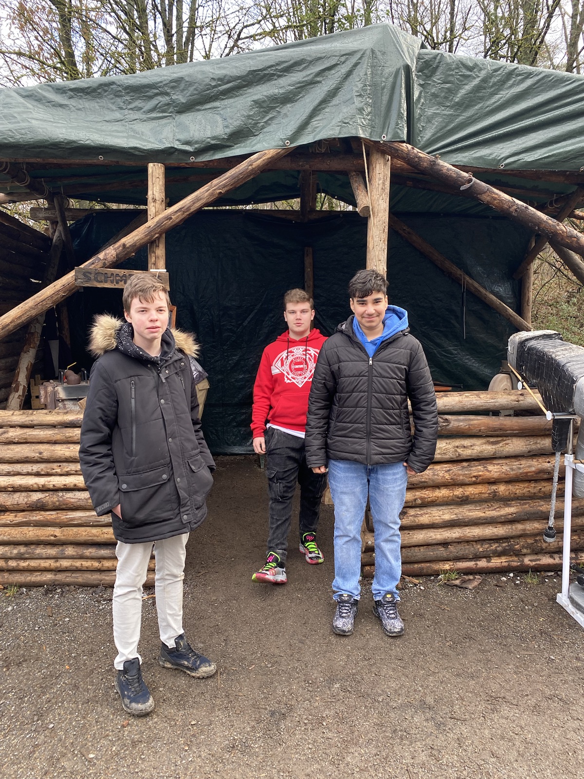 3 Schüler an einer Holzhütte